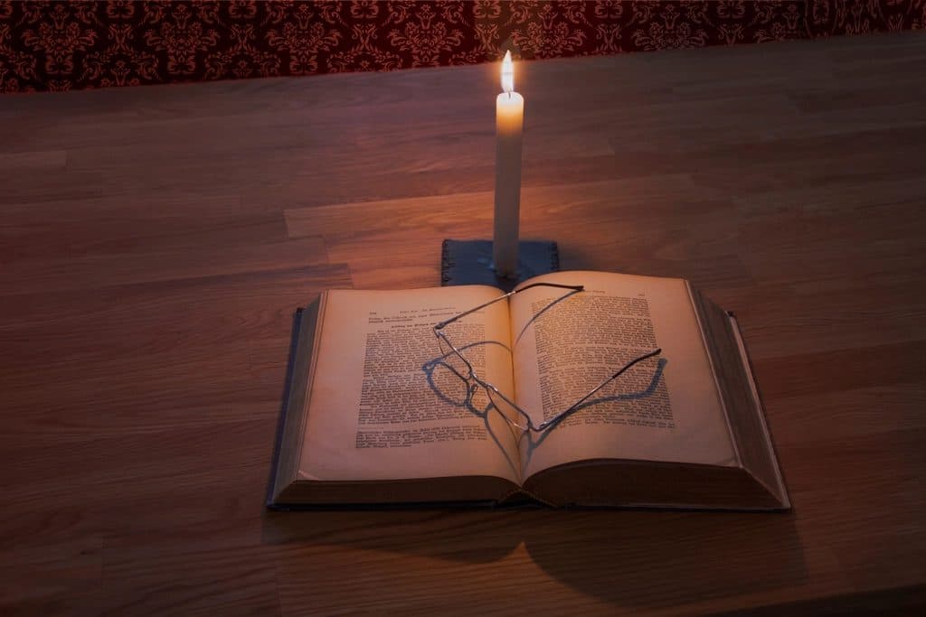 An open Bible and reading glasses lit by candlelight